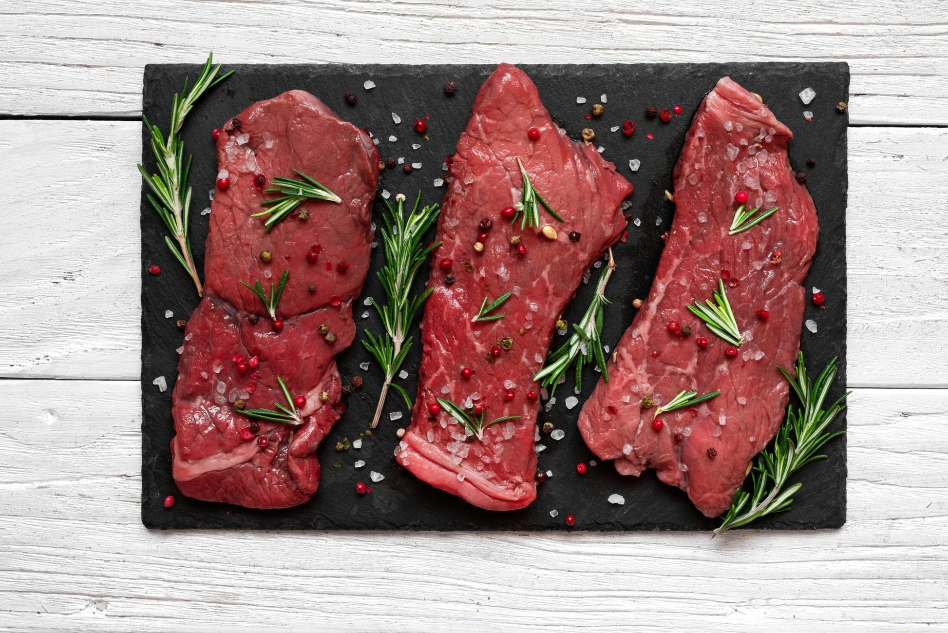 Raw meat, beef steak with spices and rosemary on black slate cutting board over wooden background